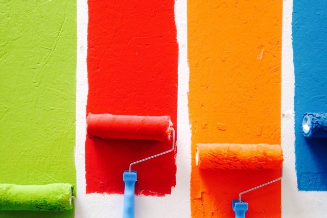 Paint rollers dipped in green, red, orange and blue paint on a wall