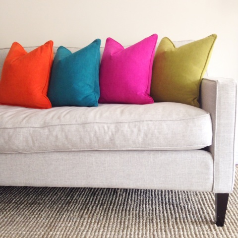 Brightly coloured cushions in orange, teal, pink and green on a grey sofa