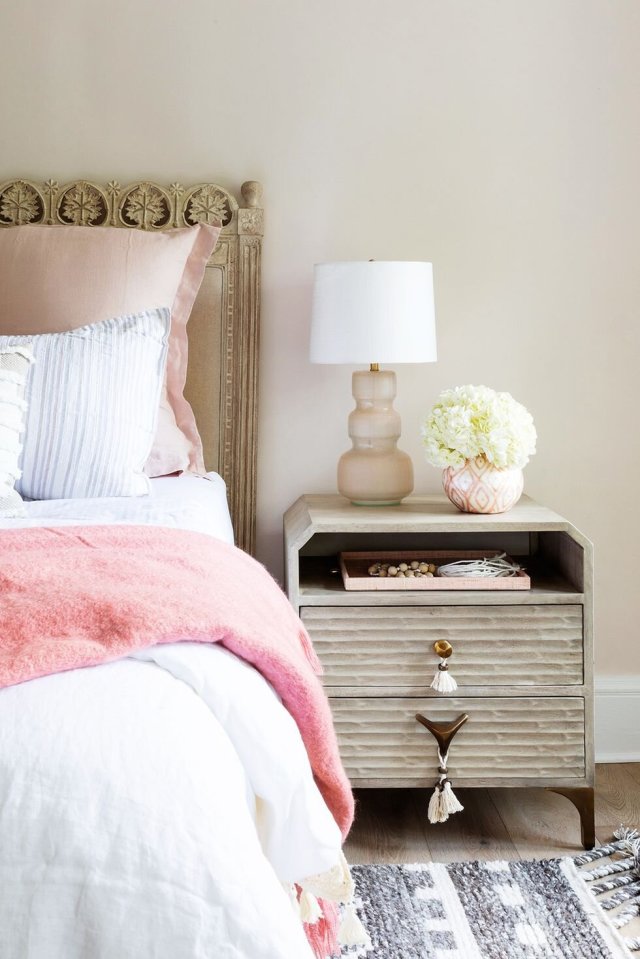 Bedside nightstand styled with a coral throw, ceramic lamp and fresh flowers